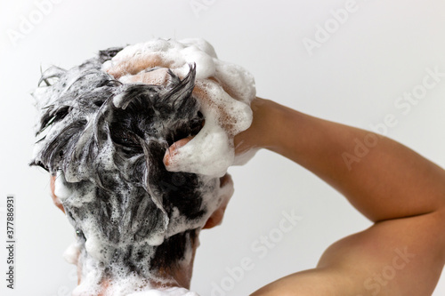 A man washes his head with shampoo on white background, rear view photo