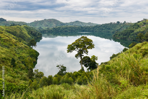 A small lake with reflected clouds on its still surface surrounded with rich vegetation and farm fields in the background near the Bwindi National Park during a cloudy day in uganda photo
