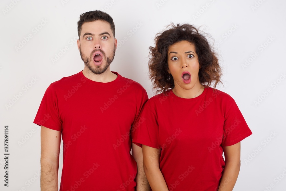 Oh my God. Surprised Young beautiful couple wearing red t-shirt on white background stares at camera with shocked expression exclaims with unexpectedness, Oh my God. Surprised Young beautiful couple wearing red t-shirt on white background stares at camera with shocked expression exclaims with unexpectedness,