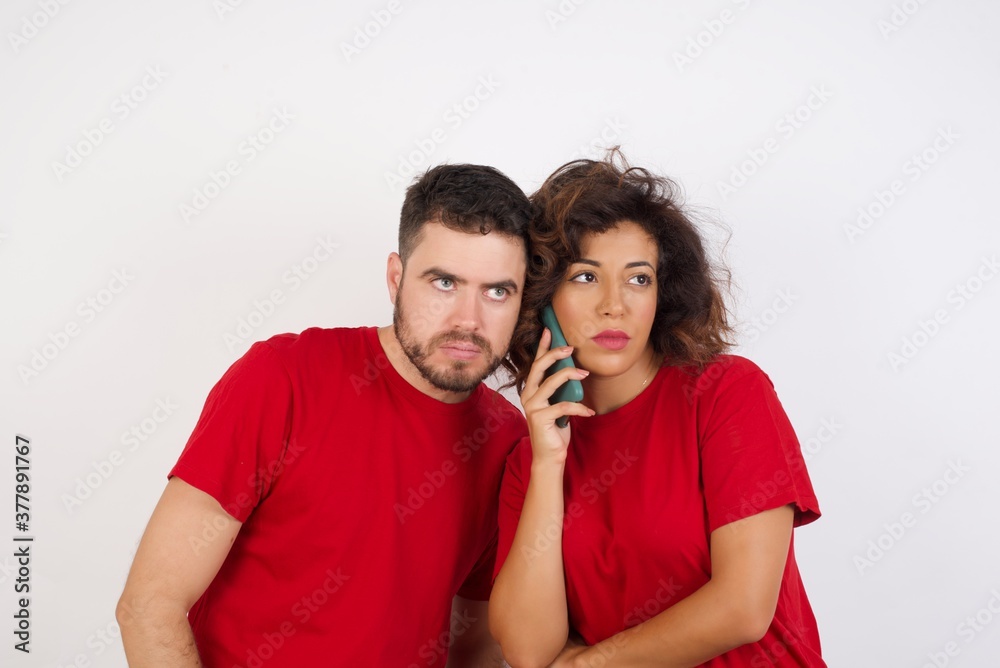 Sad Young beautiful couple wearing red t-shirt on white background talking on smartphone. Communication concept. Sad Young beautiful couple wearing red t-shirt on white background talking on smartphone. Communication concept.