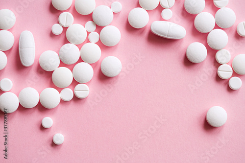 white tablets of various shapes on pink background close up top view. minimalistic concept of medicine and treatment