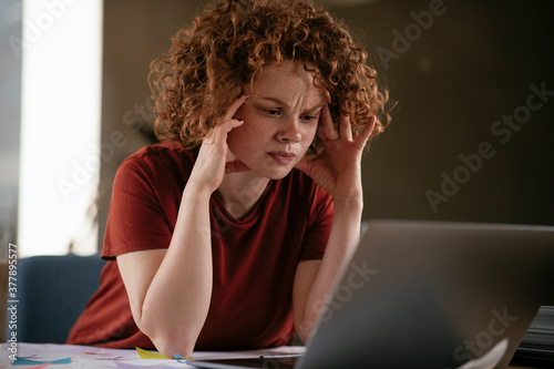 Tired businesswoman working on project. Young woman with curly hair in office..