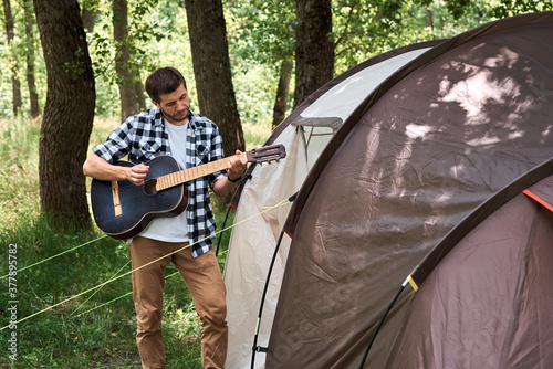 Tourist man with guitar near camping tent