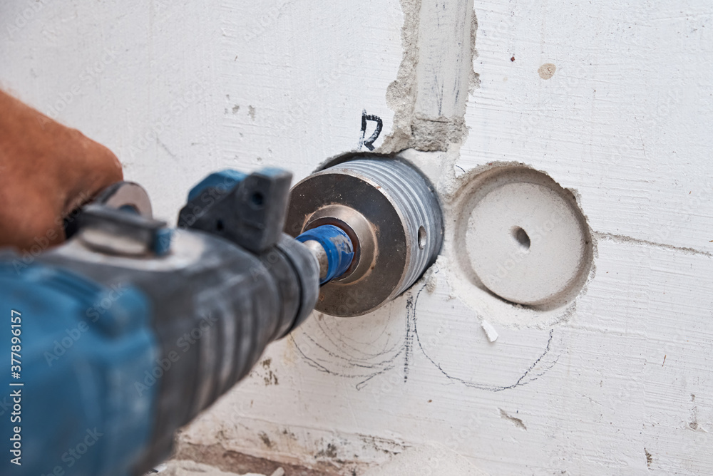 Builder with hummer drill perforator drills hole in a wall