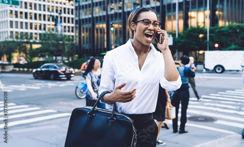 Cheerful woman in formal wear talking on phone on city street