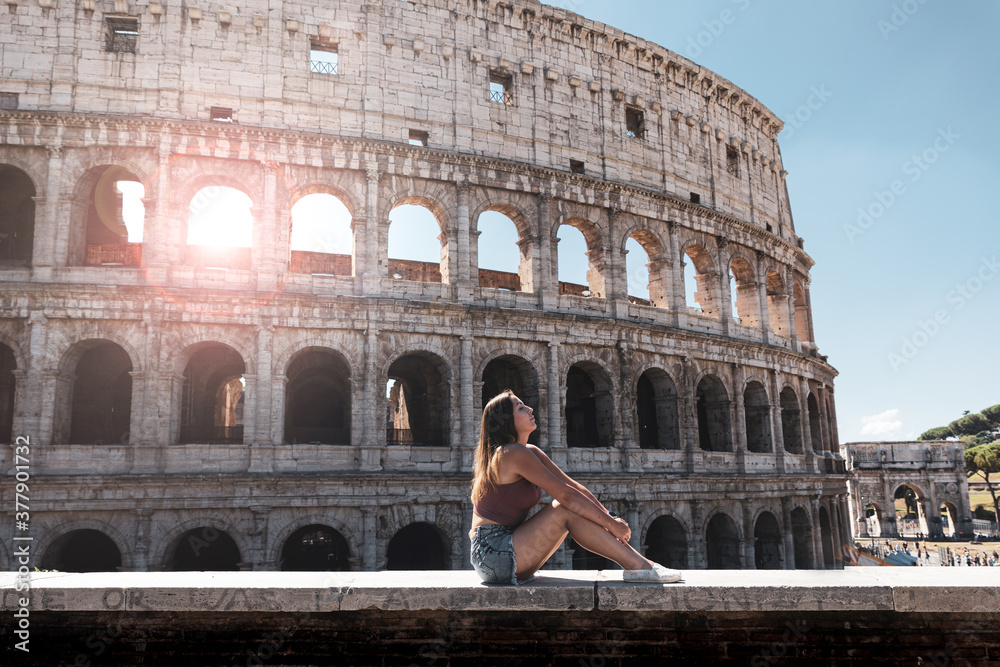 Girl is sitting on a wall on the background of the colosseum on vacation in Rome, Italy