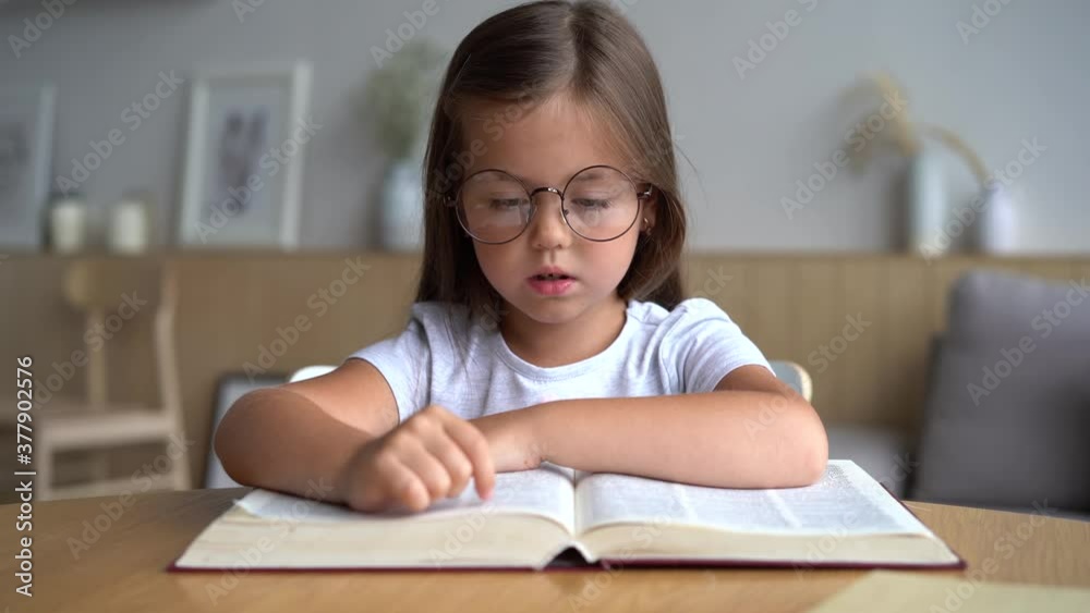 Cute smart primary school child girl reading book at home table, children elementary education concept Cute smart primary school child girl reading book at home table, children elementary education concept