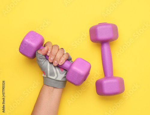 female hand in a pink sports glove holds a purple one kilogram dumbbell