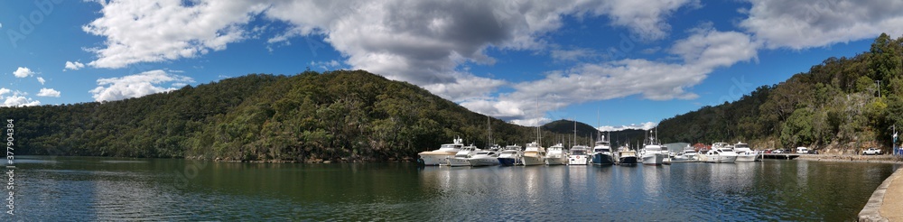 Beautiful morning  panoramic view of Cowan creek with reflections of blue sky, puffy clouds, mountains, trees and boats, Bobbin Head, Ku-ring-gai Chase National Park, New South Wales, Australia
