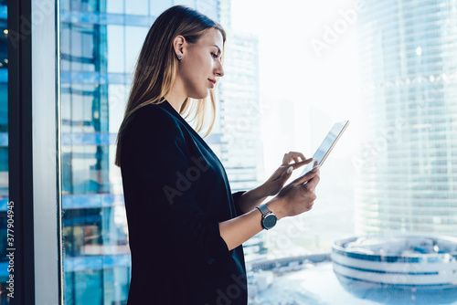 Confident professional female lawyer using app on touchpad connected to wireless internet making research in office,blonde business woman in formal wear browse via digital tablet near panoramic window photo