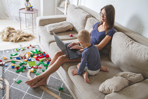 kid plays on the sofa while mom works with laptop, distracts and interferes with mom's work