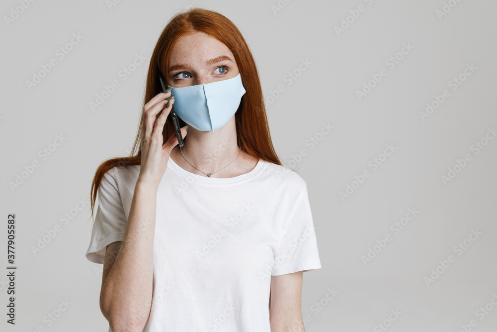 Image of nice ginger girl in face mask talking on mobile phone