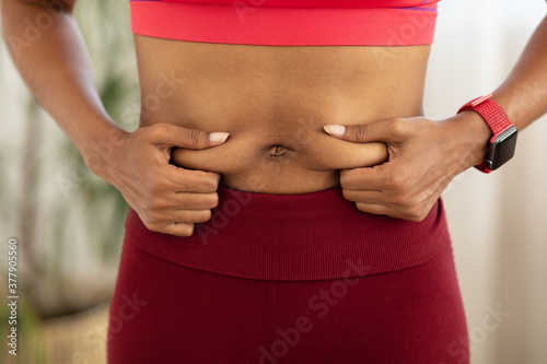 Black Woman Touching Belly Fat Losing Weight Standing Indoors, Cropped