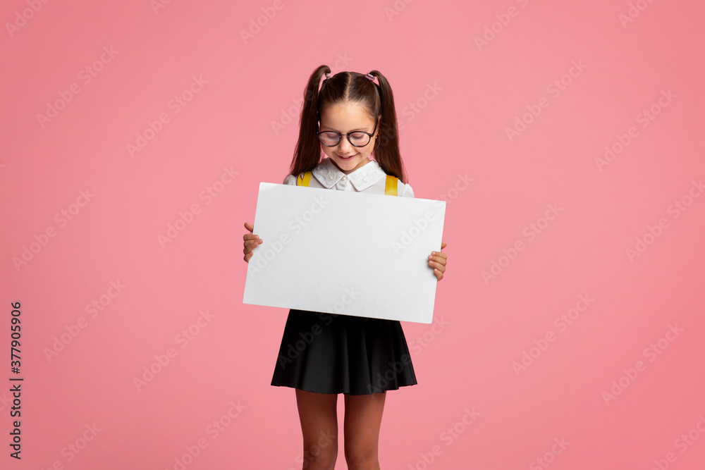 Private schooling. Small child girl in glasses and school uniform holds table with empty space Private schooling. Small child girl in glasses and school uniform holds table with empty space