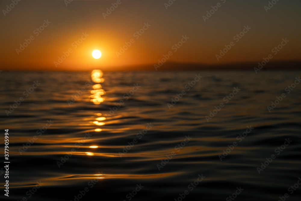 Colorful sunset or sunrise at sea with focus on waves at foreground 