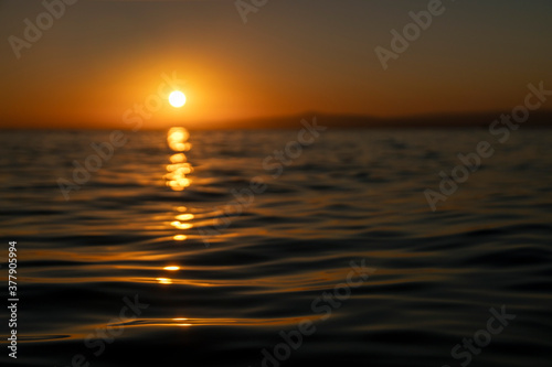 Colorful sunset or sunrise at sea with focus on waves at foreground 