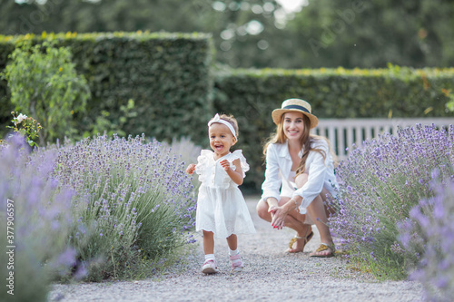 Beautiful young mother and her little daughter in blooming lavender. International family. Mom and daughter in the sunset. Summer.