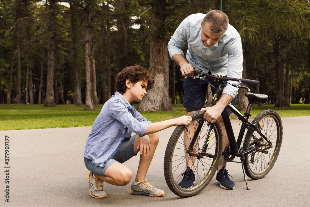Closeup portrait of focused dad and son checking bike Closeup portrait of focused dad and son checking bike