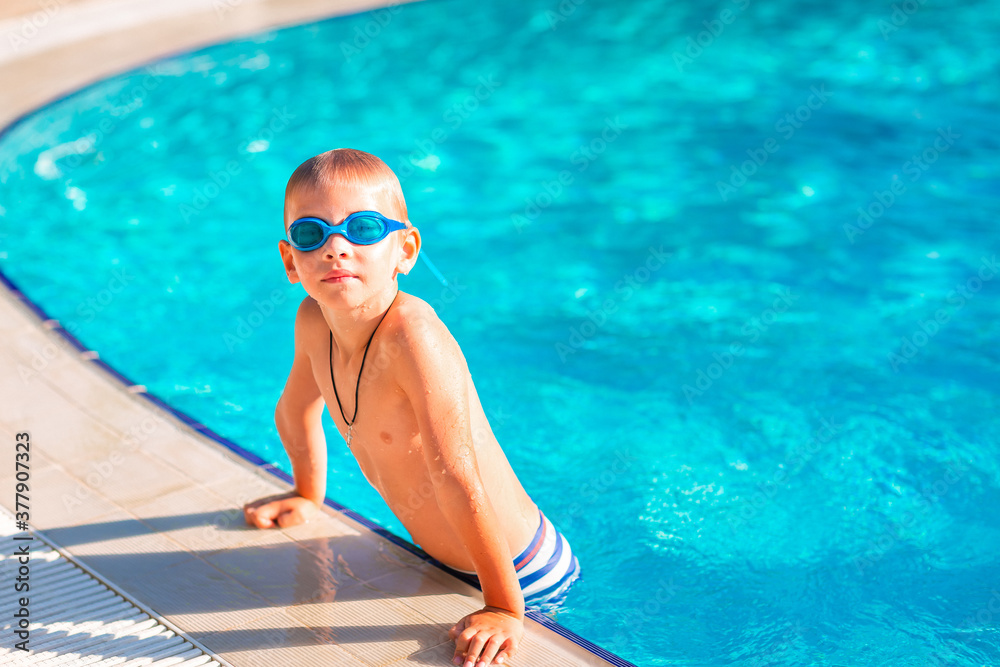 Cute happy little boy in goggles swimming in the swimming pool