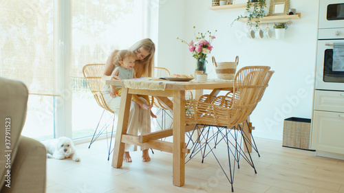 Young beautiful mother spending time with baby daughter in dining room at home. 