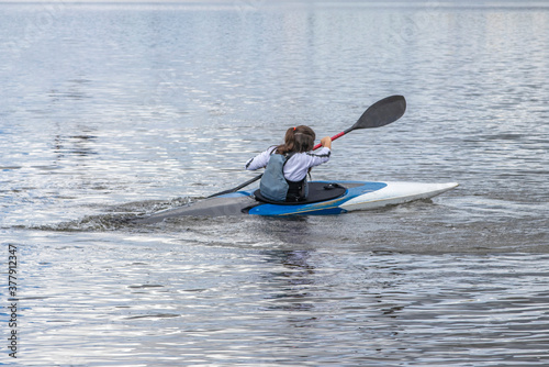 A young girl trains in water sports, kayaking, canoeing. In her hands she is holding an oar with which she is rowing.