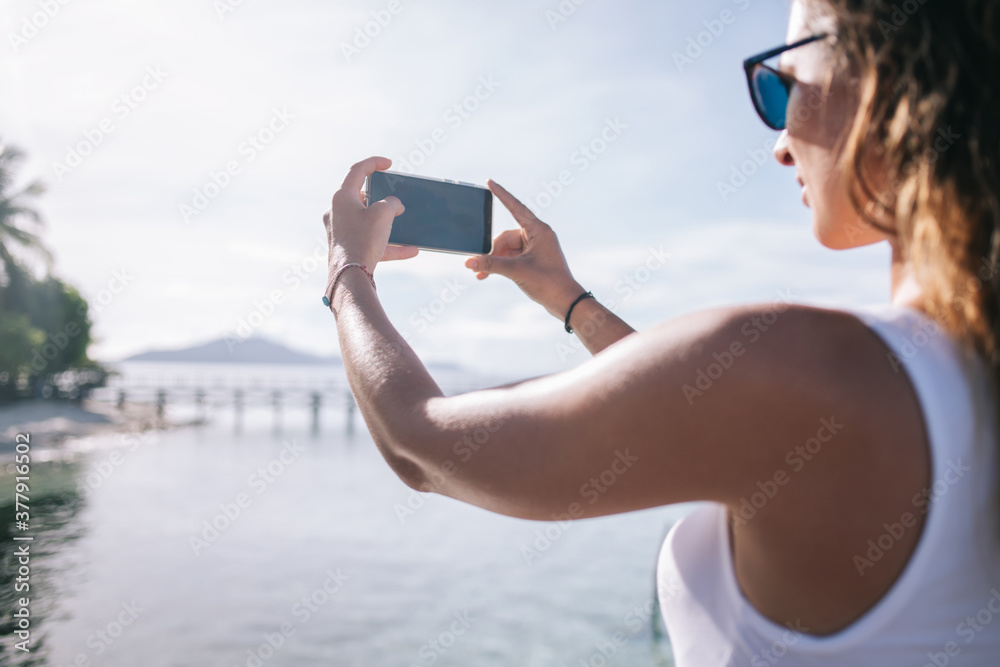 Millennial tourist using smartphone camera for photographing coastline scenery during recreation vacations on Bahamas, female traveller shooting video vlog about getaway journey on Philippines