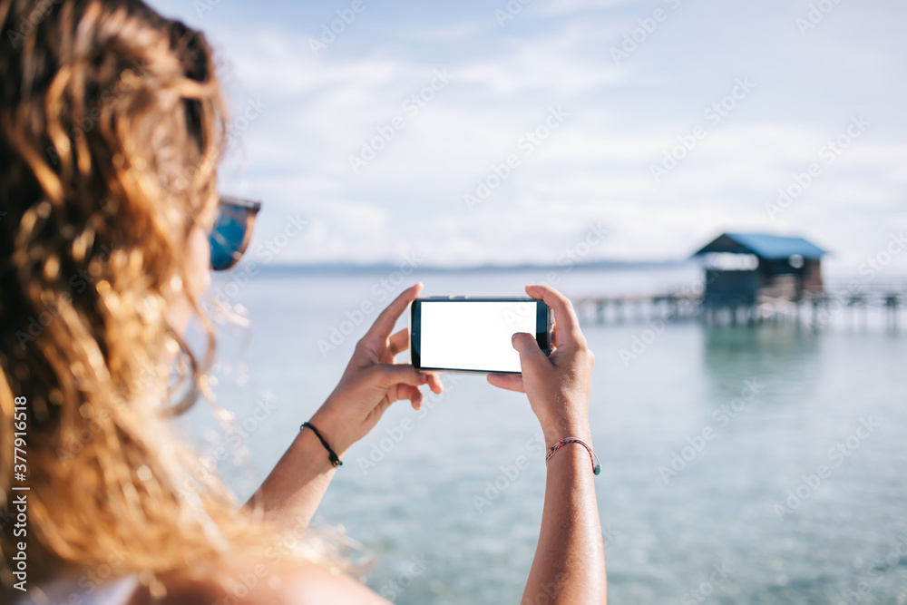 Traveling woman using smartphone for taking photo of sea