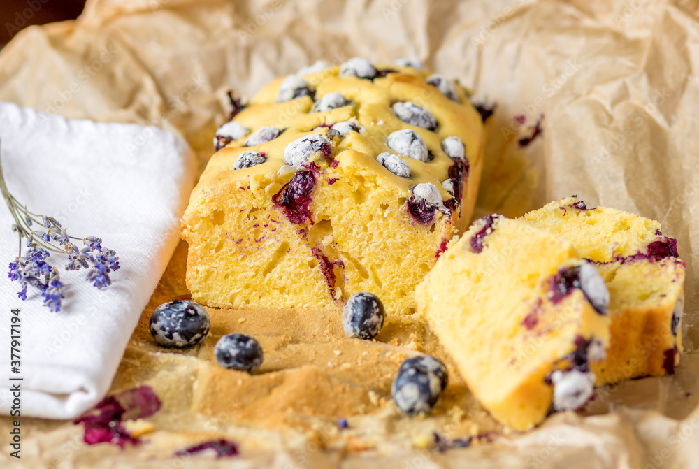 Selective focus to the soft yogurt plumcake with blueberries on baking paper at the table.