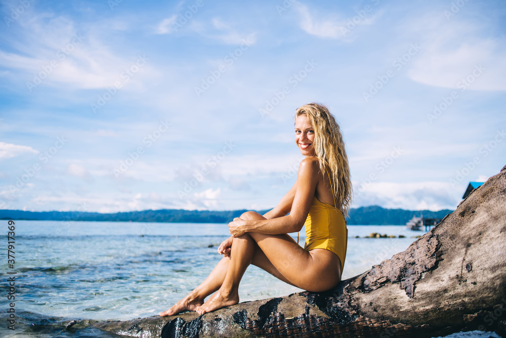 Young blonde sitting on dead tree and looking at camera on beach Young blonde sitting on dead tree and looking at camera on beach