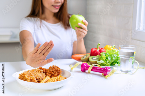 Close up of young Asian woman using hand push out her favourite fried chicken, french fries and choose green apple, vegetables for good health. Woman on dieting concept. Close up