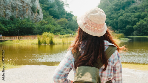 Cheerful young traveler Asian lady with backpack walking at the mountain lake. Korean teen girl enjoy her holidays adventure feeling happy freedom. Lifestyle travel and relax in free time concept.