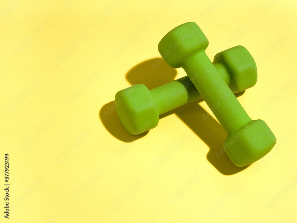 Two green dumbbells on yellow background. Two green dumbbells on yellow background.