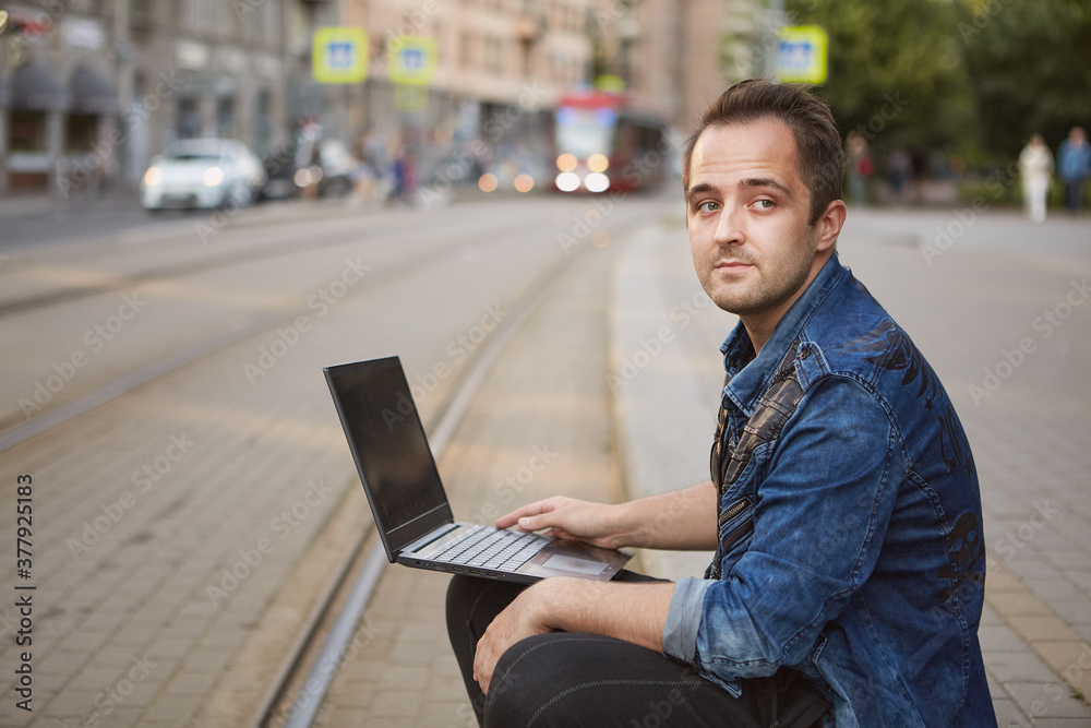 Man with laptop sits near railroad track.