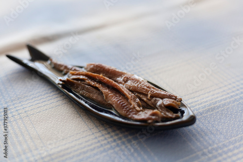 Canned anchovies caught in the Cantabrian Sea plated in a blue fish shaped plate served on a blue squared tablecloth. Anchovy is a typical high quality delicious tapas dish from the northern Spain.
 photo