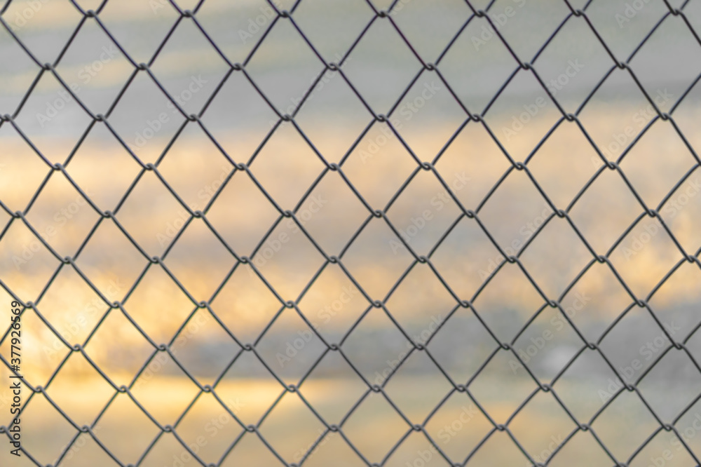 The blurred background of a gray iron door crossed into equally spaced rhombus panels. The backdrop of the orange sky as the sunsets. Feeling safe and secure. Idea for grid wallpaper with copy space. The blurred background of a gray iron door crossed into equally spaced rhombus panels. The backdrop of the orange sky as the sunsets. Feeling safe and secure. Idea for grid wallpaper with copy space.