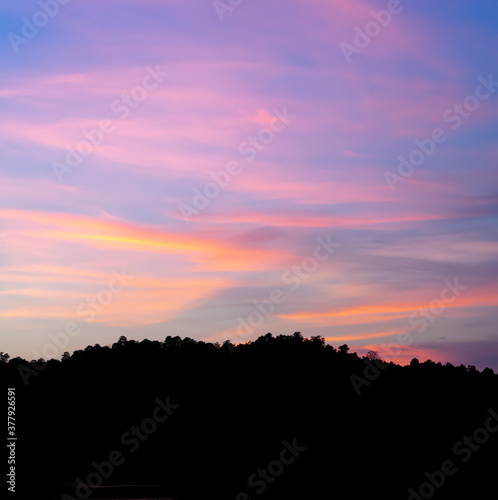A photograph of clouds pattern in the twilight colored sky in the evening. The bellow edge of the image is a black large mountain. Feeling calm, relax, and romantic. There is a copy space on top.