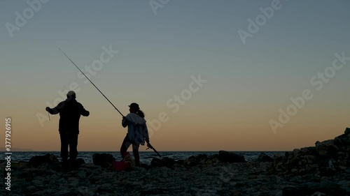 two people fishermen a man and a woman fishing at sunset on the stone shore