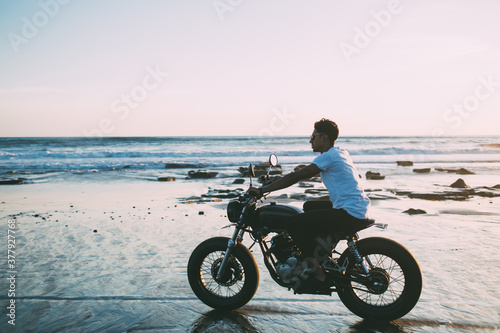 Young male biker sitting on motorcycle on beach