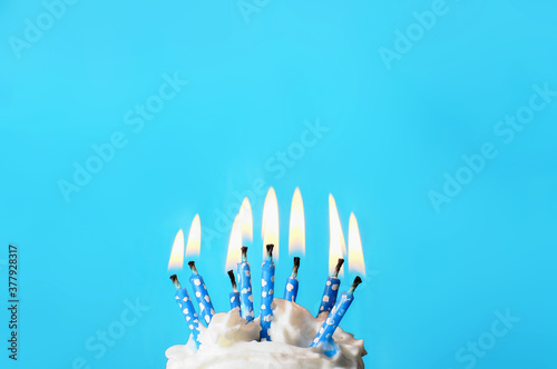 cream cake with blue candles on top, the candles have white dots and are  lit. before a light blue background. photo