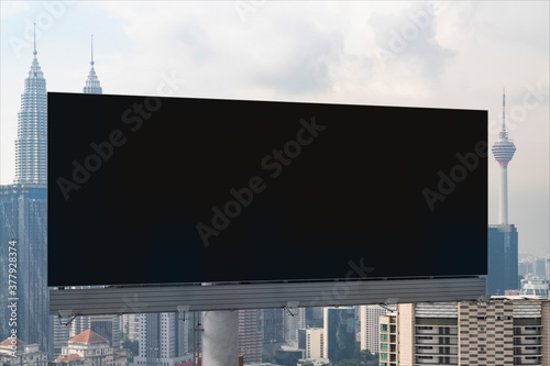 Blank black road billboard with Kuala Lumpur cityscape background at day time. Street advertising poster  mock up  3D rendering. Front view. Concept of marketing to promote or sell services or ideas.