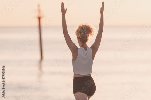 A young girl performs yoga exercises in front of the sea at sunrise