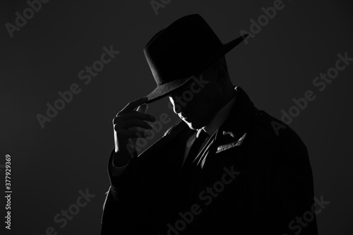 Old fashioned detective in hat on dark background, black and white effect photo