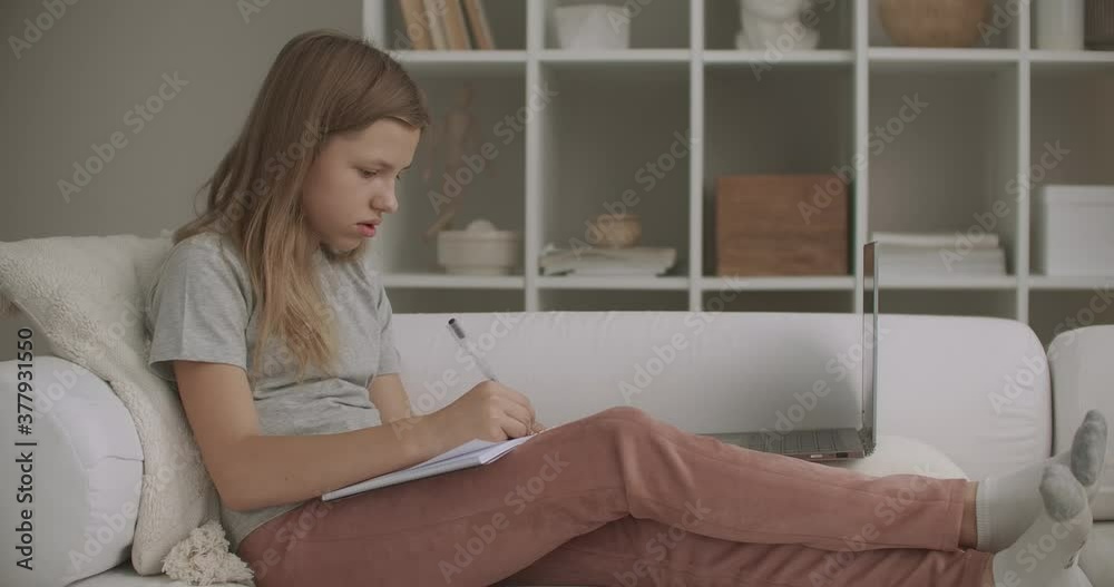 teen girl is writing in copybook, sitting at home in living room on couch at weekend, relax at vacation or weekend teen girl is writing in copybook, sitting at home in living room on couch at weekend, relax at vacation or weekend