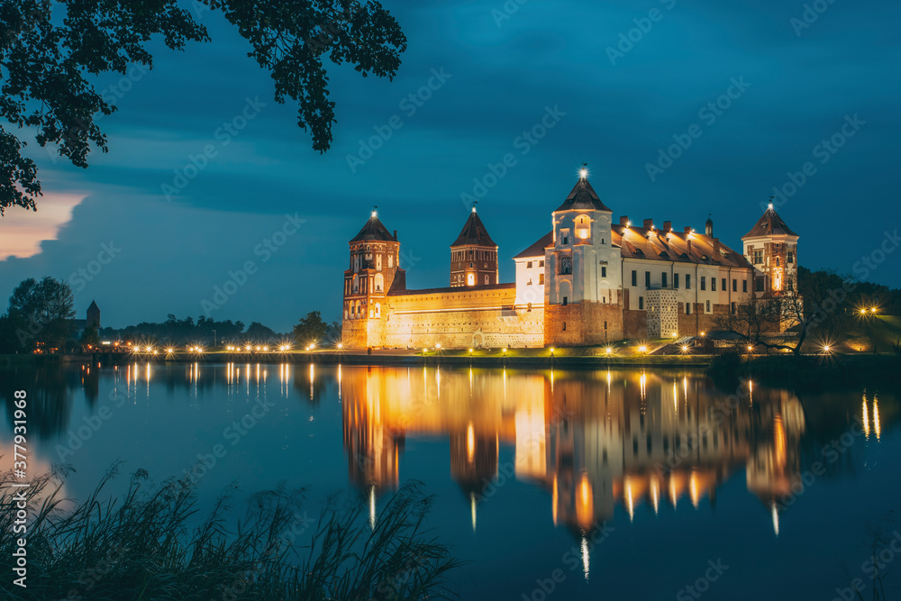 Mir, Belarus. Night Scenic View Of Mir Castle In Evening Illumination With Glow Reflections On Lake Water. UNESCO Heritage Site. Famous Landmark