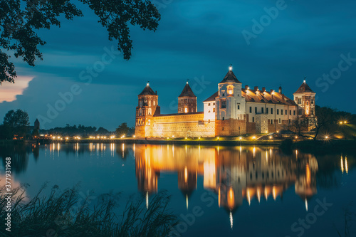 Mir, Belarus. Night Scenic View Of Mir Castle In Evening Illumination With Glow Reflections On Lake Water. UNESCO Heritage Site. Famous Landmark