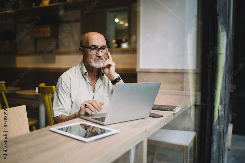 Thoughtful senior businessman working on laptop in cafe