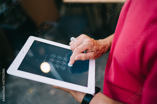 Crop faceless aged man dialing password on tablet