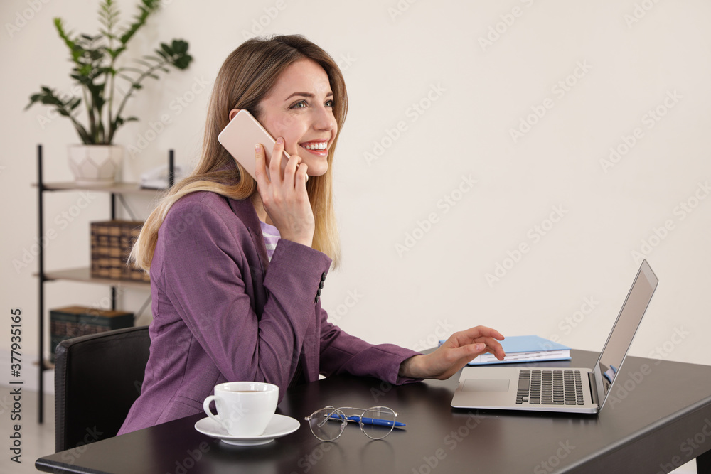 Young woman talking on phone while using laptop in office Young woman talking on phone while using laptop in office