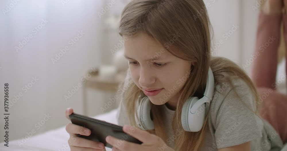 school girl is surfing internet by smartphone and viewing pictures on screen, lying on bed in home, swipping and tapping on sensor display school girl is surfing internet by smartphone and viewing pictures on screen, lying on bed in home, swipping and tapping on sensor display
