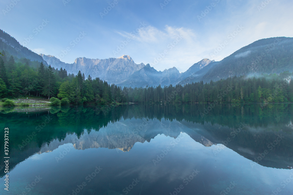 Mirror reflection in Lago di Fusine, Italy. Summer spring colors and Mangart mountain in the background at sunrise in Italien Alps.Beautiful peaceful nature scenery,turquoise water,travel background.
